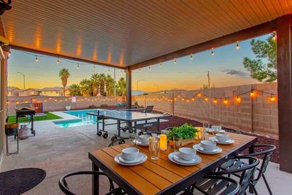 Une terrasse extérieure avec une piscine, des guirlandes lumineuses et une table dressée pour le repas.