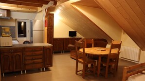 A cozy attic bedroom with a wooden dining table and chairs, a bed, and a kitchenette with a refrigerator and microwave. - chalet-style apartment, 5 minutes from the ski slopes (Les Rousses)
