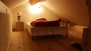 A small, cozy attic bedroom with a wooden floor, a single bed, a nightstand with a lamp, and a small chair. - chalet-style apartment, 5 minutes from the ski slopes (Les Rousses)