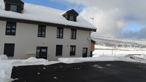 A two-story building with a snow-covered roof and a black driveway. - chalet-style apartment, 5 minutes from the ski slopes (Les Rousses)