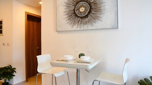 Ein Essbereich mit einem Tisch für zwei Personen, zwei weißen Stühlen, einer Wanddekoration und einem Blumentopf.