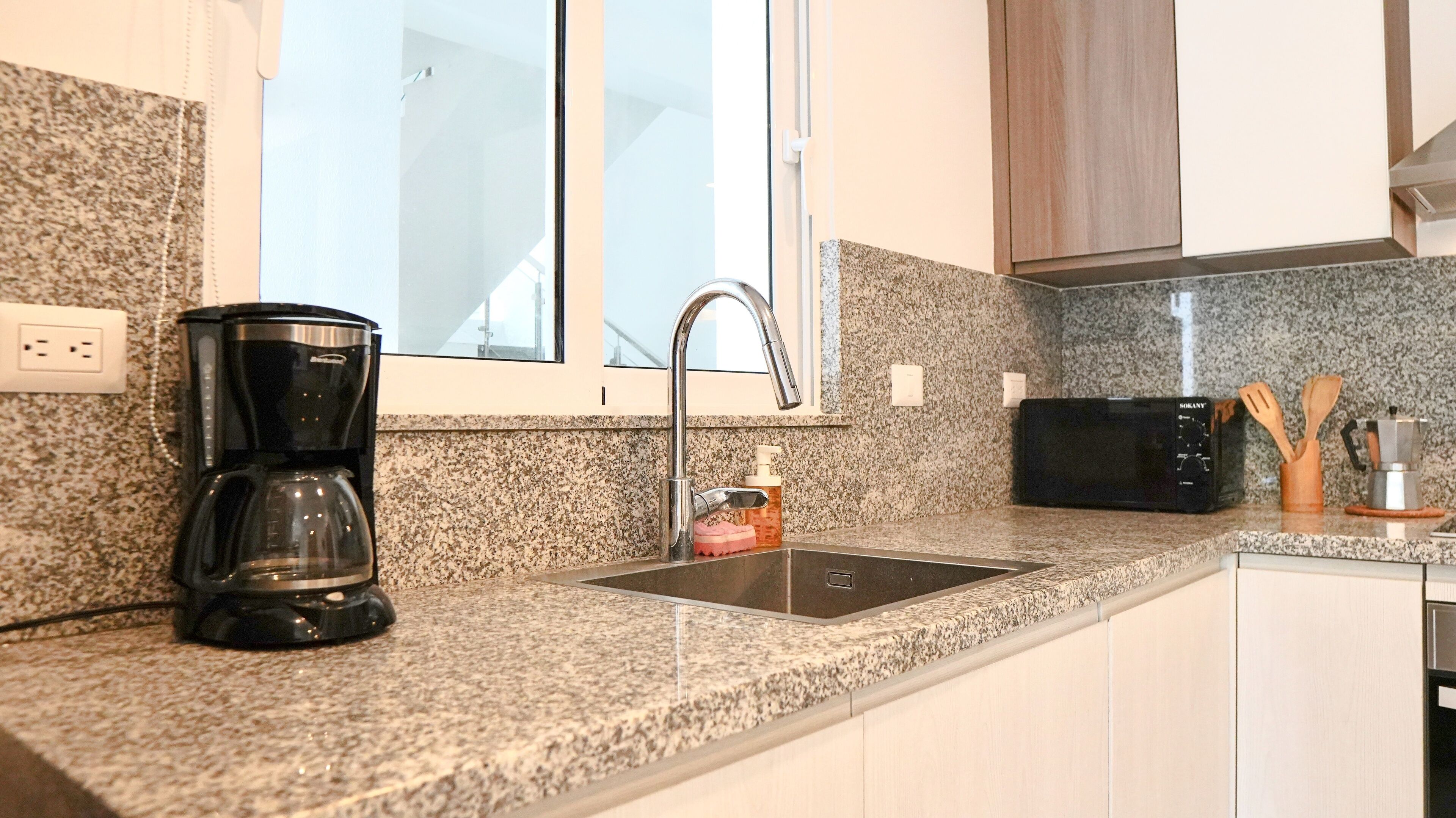 A kitchen with granite countertops, a coffee maker, a microwave, and a sink.