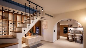 Ein modernes Interieur mit einer Treppe zu einem Erkerbereich, einer Küche mit Barhocker und einem Essbereich mit großem Fenster.