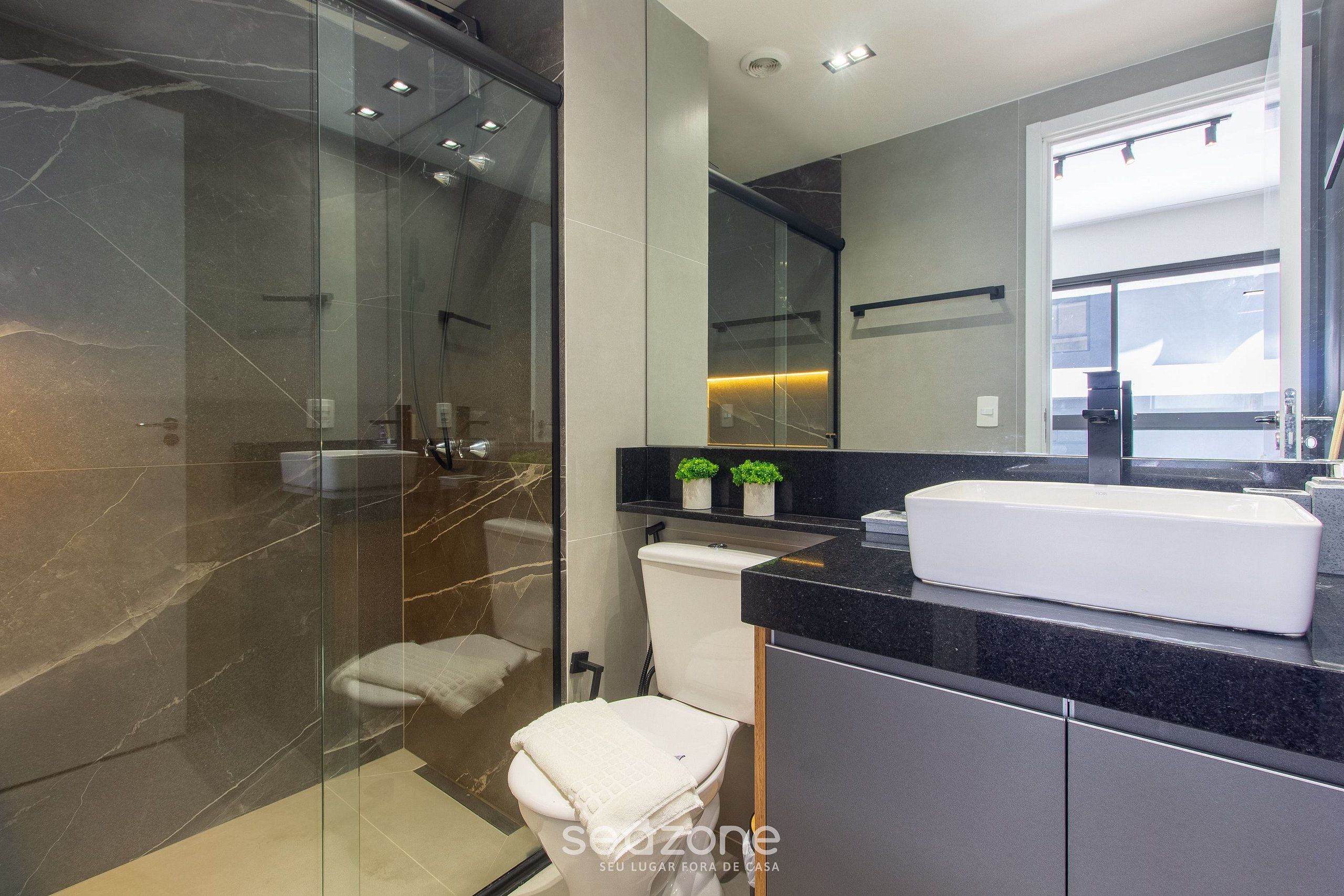 A modern bathroom with a glass-enclosed shower, a white toilet, and a black countertop with a white sink.
