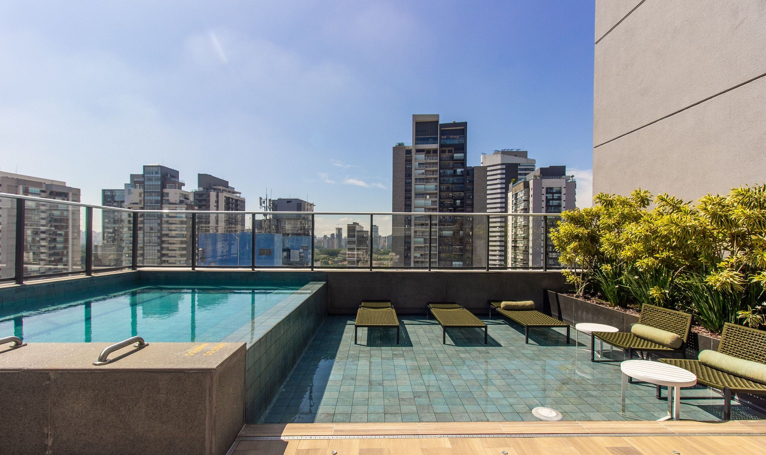 A rooftop pool with a city view, lounge chairs, and a small table.