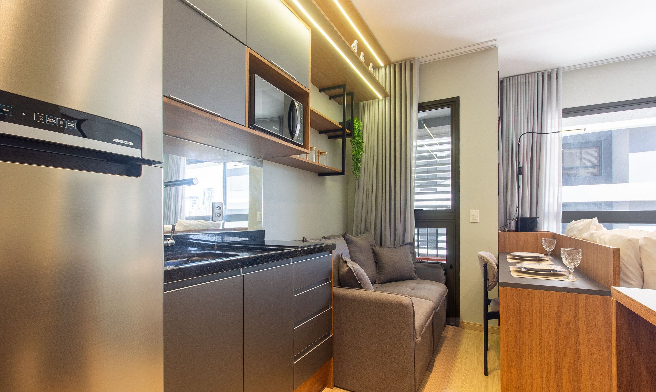 Een functionele keuken met een ingebouwde magnetron, een eethoek met tafel en stoelen, en een zithoek met een bank.