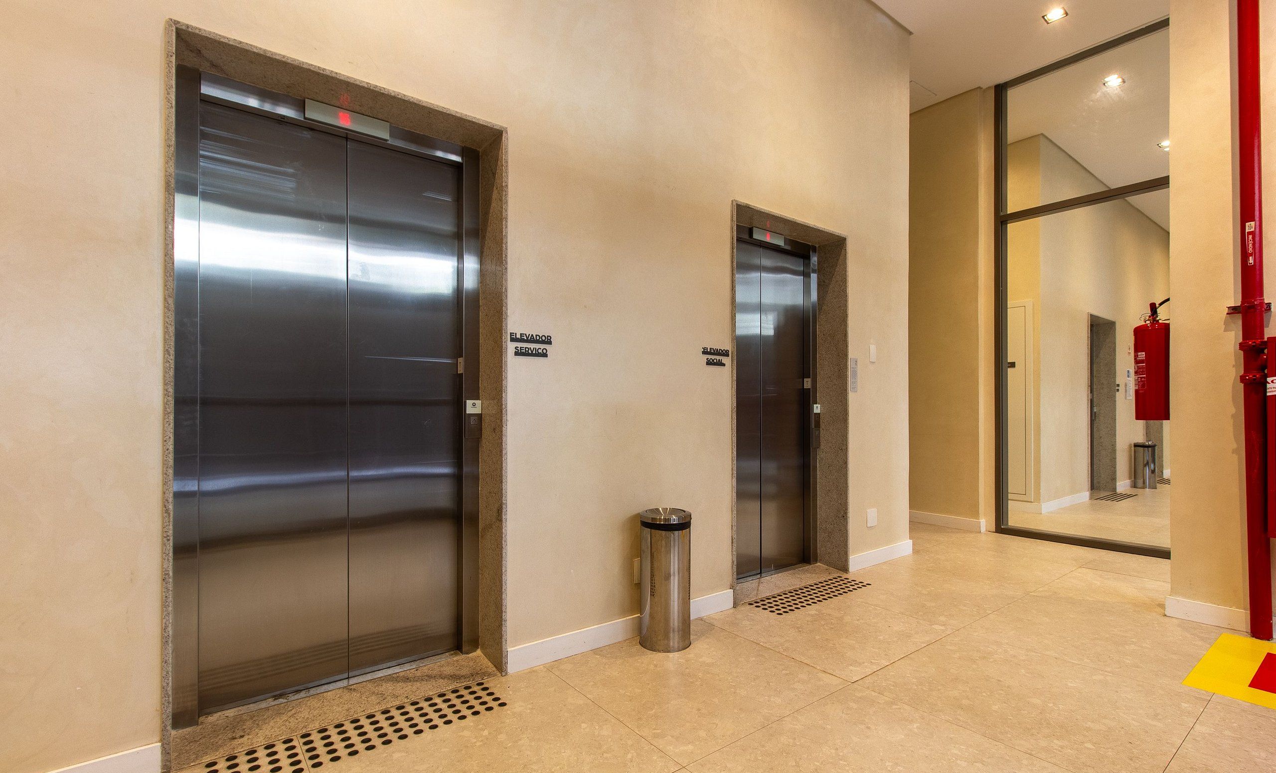 A modern elevator area with two elevators, a trash bin, and a fire extinguisher.