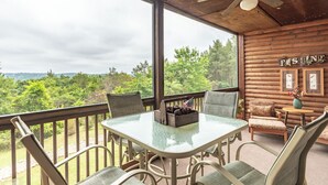 A wooden cabin with a glass table and chairs, a ceiling fan, and a view of the forest. - 2BR Village At Indian Point 501 near SDC-Free Tickets Daily up to $500 (Branson)