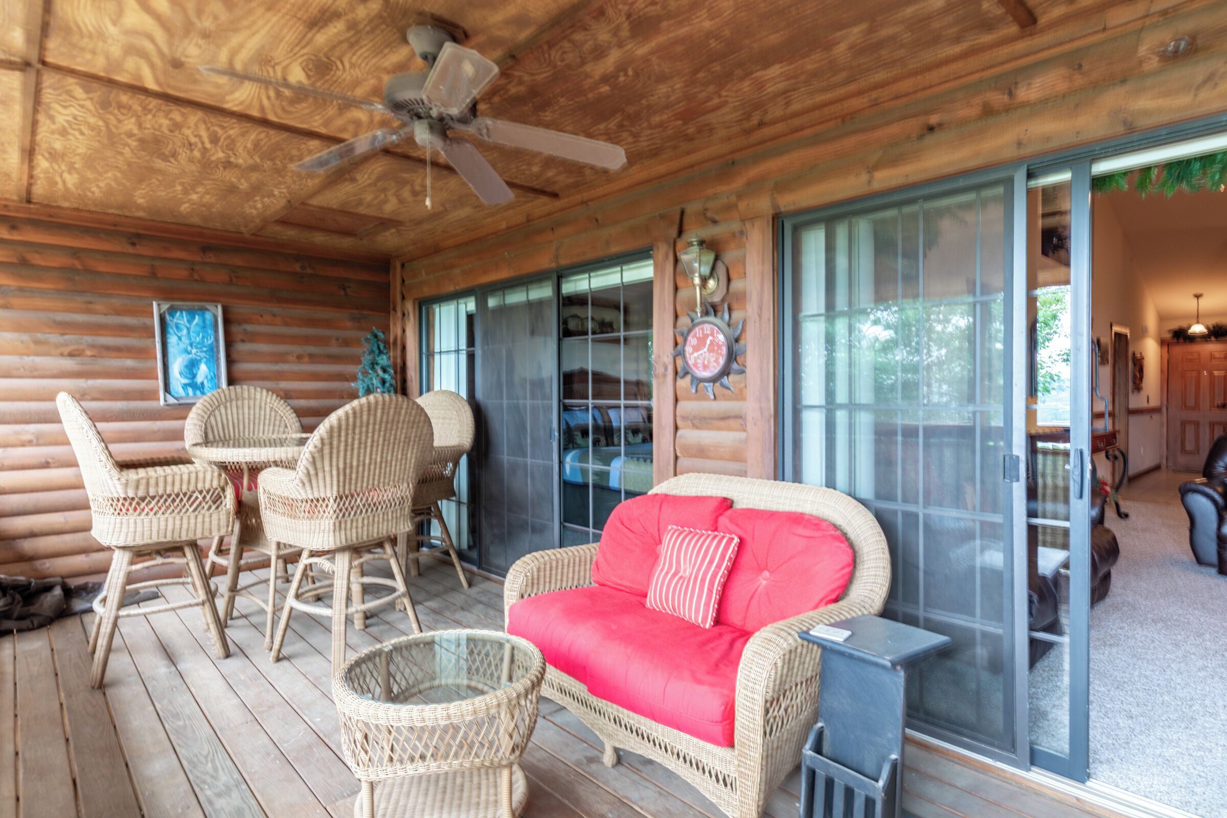A wooden deck with wicker furniture, a glass door leading to a room, and a ceiling fan.