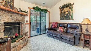 A cozy living room with a stone fireplace, a leather sofa, a large bear painting, and a glass door leading to a balcony. - 2BR Village At Indian Point 0611 near SDC-Free Tickets Daily up to $500 Value (Branson)