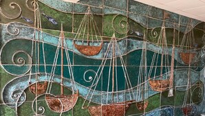 Een mozaïekwand met een maritiem thema, waarin schepen en golven afgebeeld zijn.
