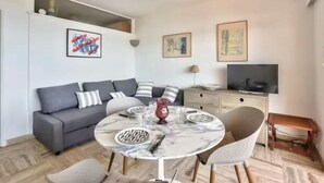 Een moderne woonkamer met een grijze bank, een ronde marmeren tafel en een televisie op een houten dressoir.