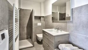 Een moderne badkamer met een inloopdouche, toilet, wastafel met spiegel en een handdoekhouder.
