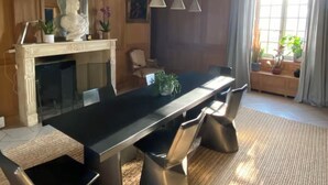 A modern dining area with a long table, black chairs, hanging pendant lights, and a fireplace. - Suite d'hôtes - Domaine de Poulaines (Poulaines)