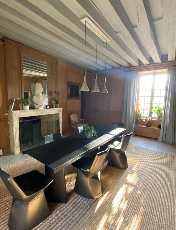 A modern dining area with a long table, black chairs, hanging pendant lights, and a fireplace. - Suite d'hôtes - Domaine de Poulaines (Poulaines)