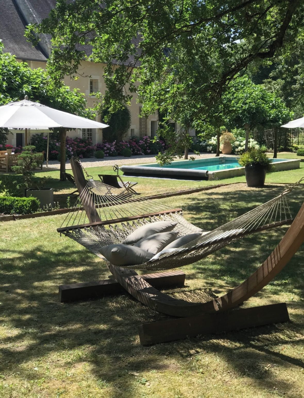 A hammock in a garden with a pool and a building in the background.