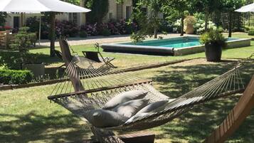 A hammock in a garden with a pool and a building in the background.