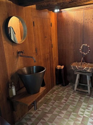 A rustic bathroom with a large metal basin, wooden walls, a mirror, and a patterned floor. - Suite d'hôtes - Domaine de Poulaines (Poulaines)