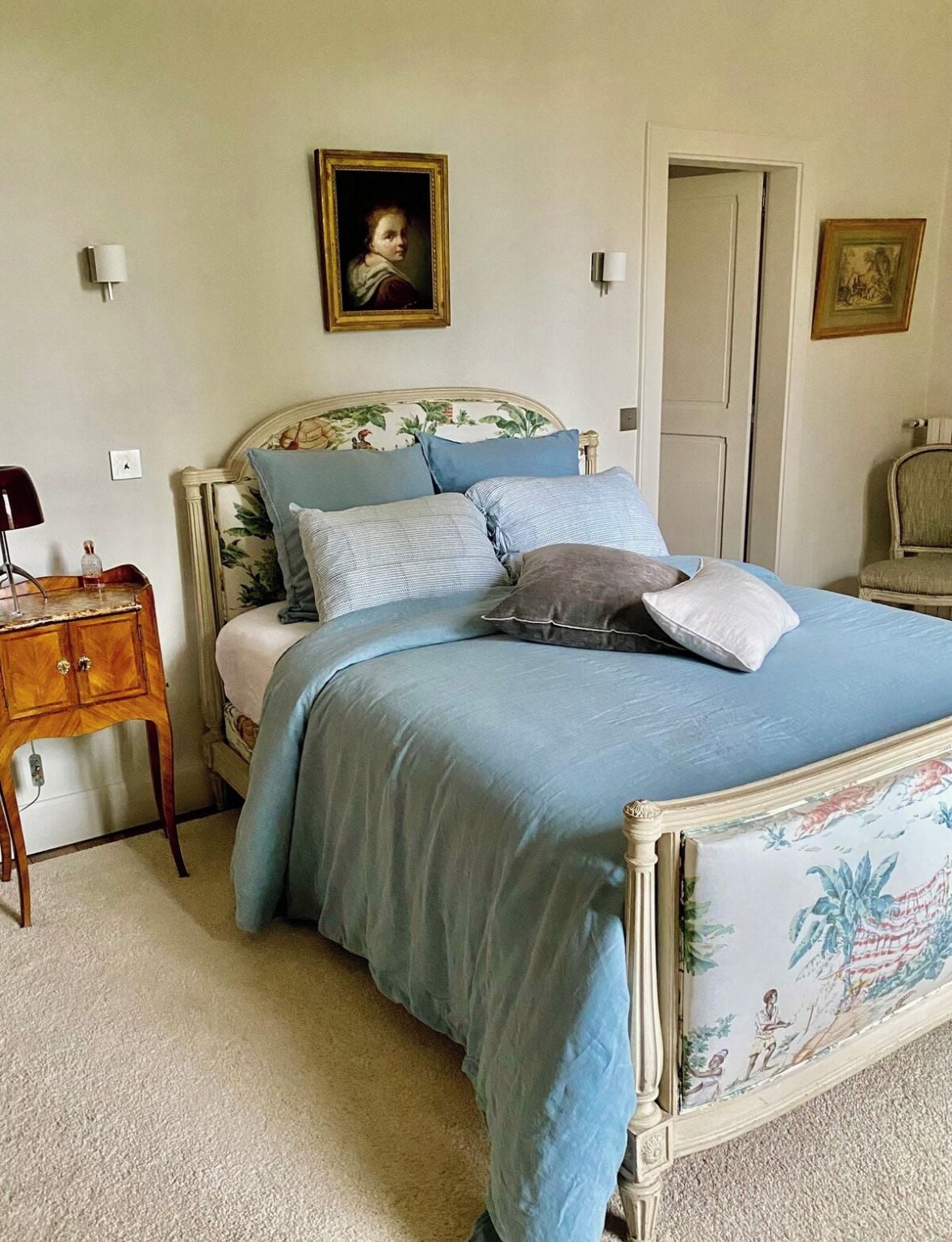 Een slaapkamer met een bed, een nachtkastje, een stoel en twee schilderijen aan de muur.