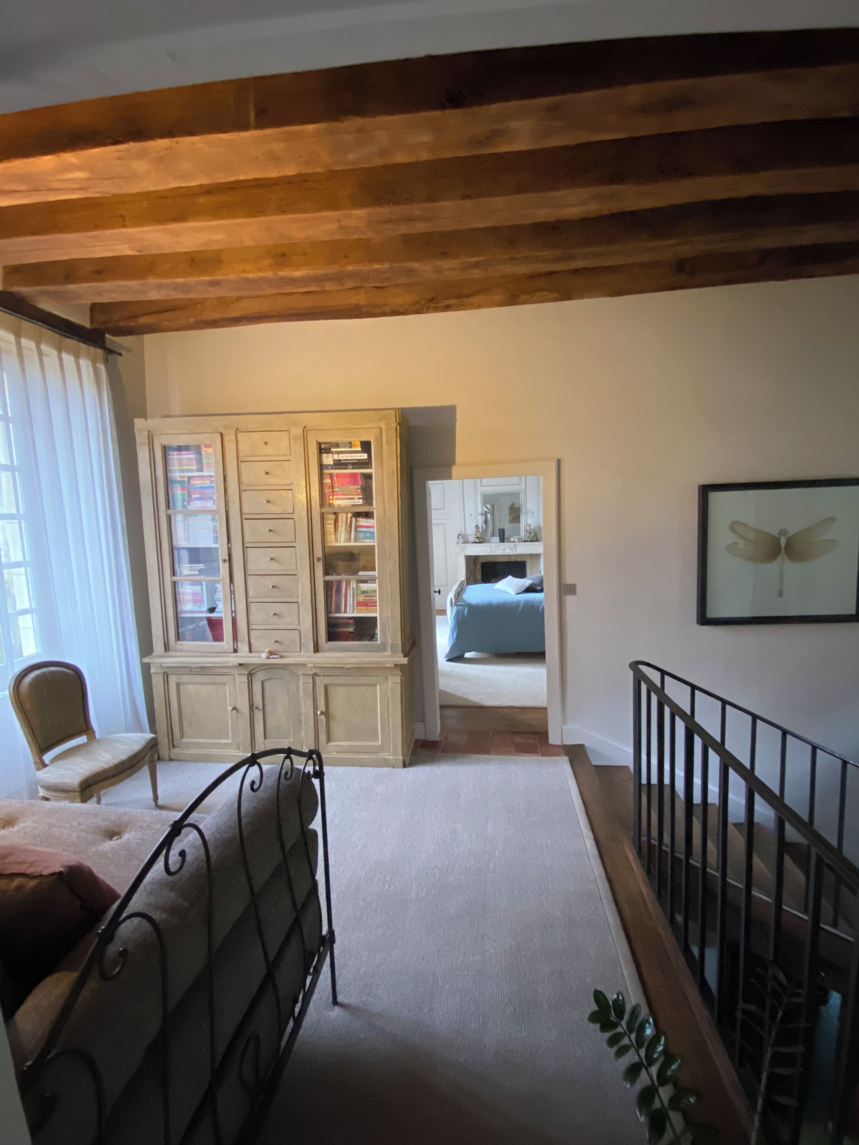 A room with a bed, a chair, a bookshelf, and a staircase.