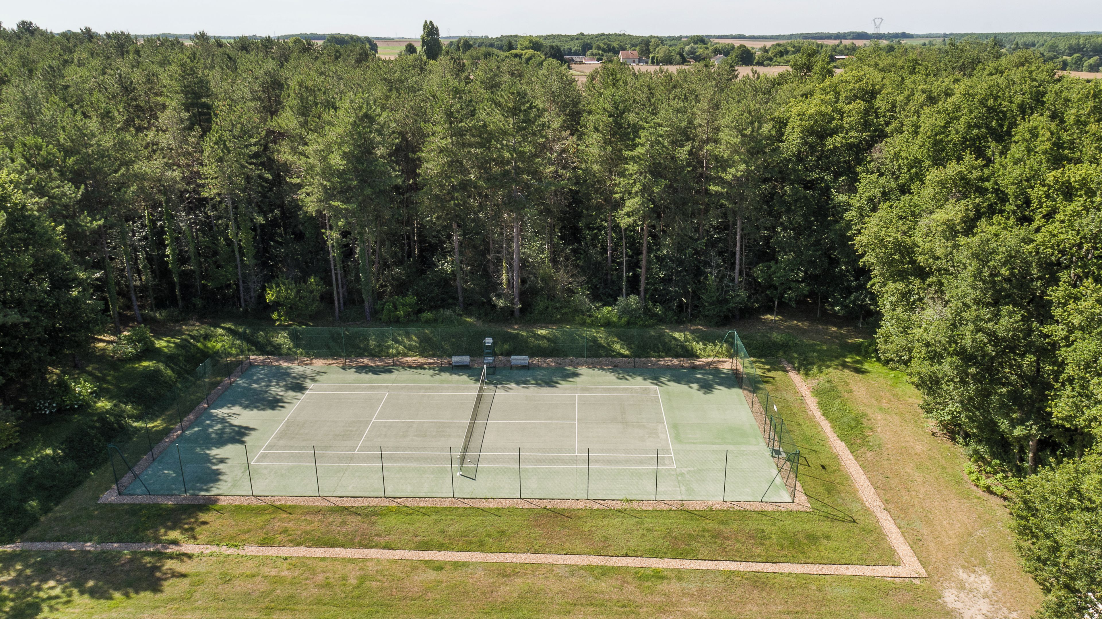A tennis court surrounded by dense trees.