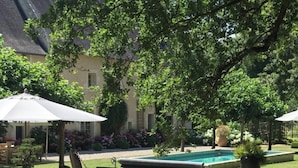 A hammock in a garden with a pool and a building in the background. - Suite d'hôtes - Domaine de Poulaines (Poulaines)