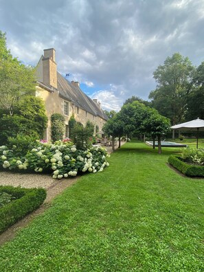 A well-maintained garden with a variety of plants and a building with a brick facade. - Suite d'hôtes - Domaine de Poulaines (Poulaines)