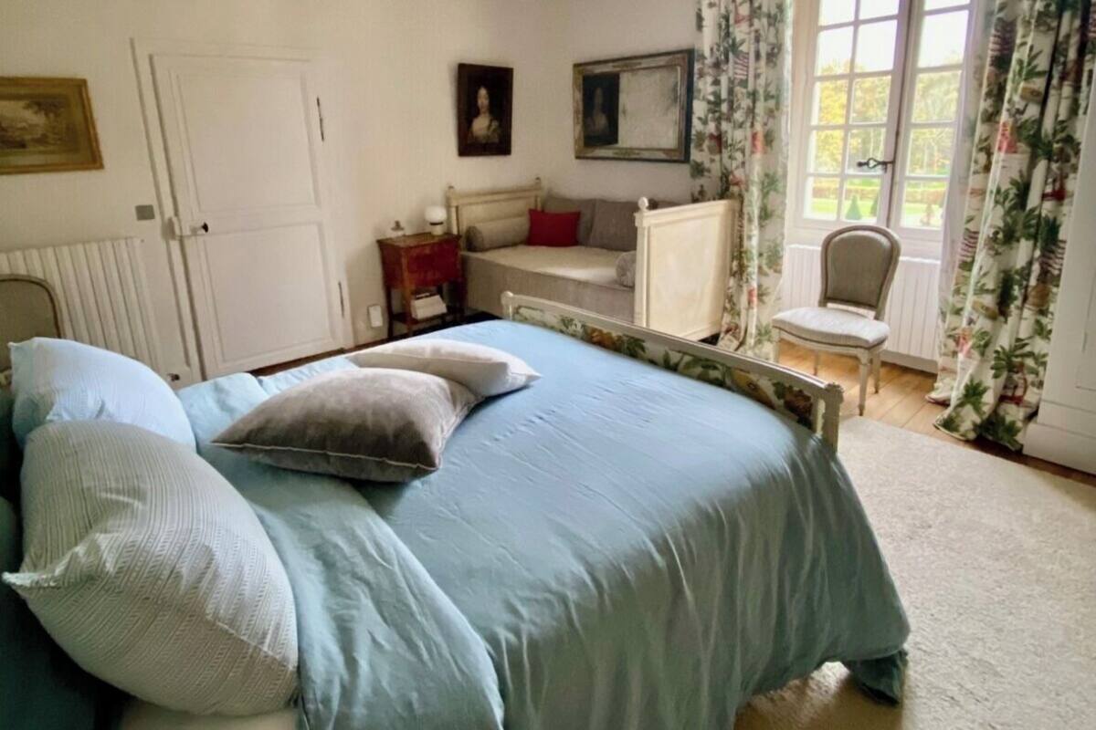 A bedroom with a bed, a chair, a window with curtains, and a door.