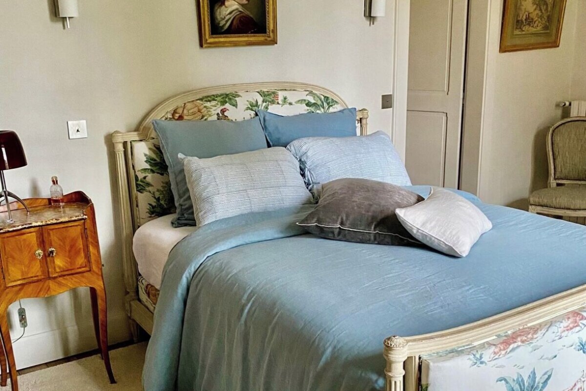 A bedroom with a bed, a nightstand, a chair, and two paintings on the wall.