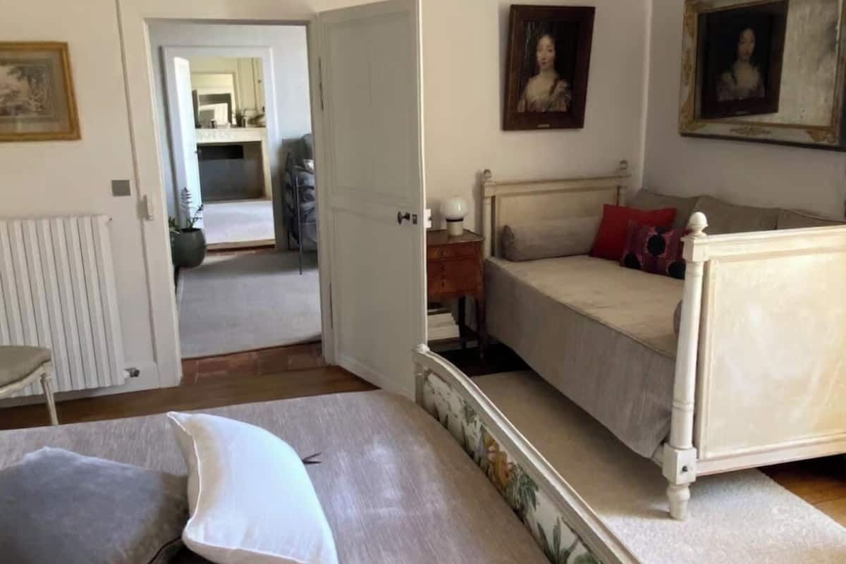 A bedroom with a bed, a chair, a radiator, and a door leading to another room.