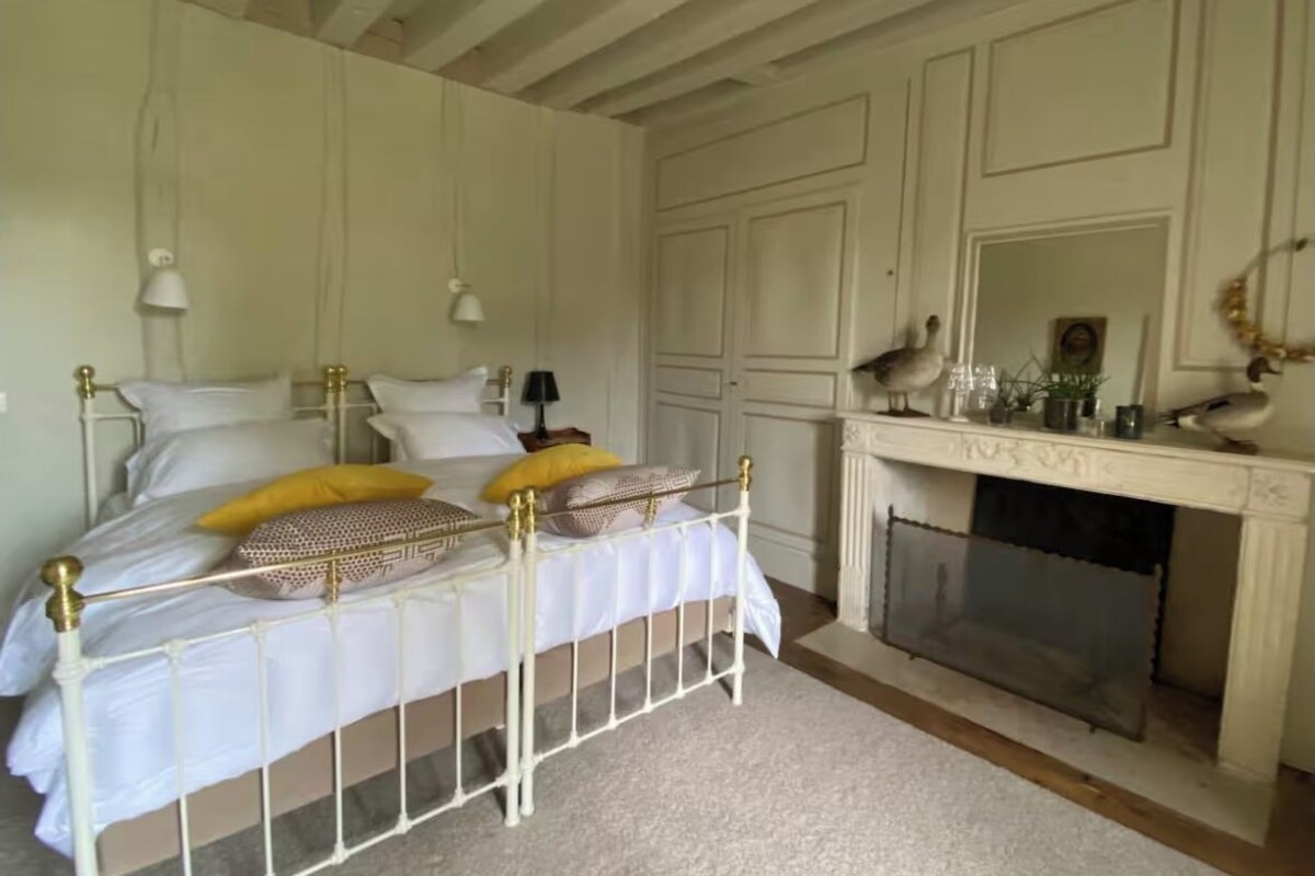 A bedroom with a bed, bedside lamps, a fireplace, and a mirror.
