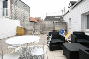 En terrasse med et rundt bord og stole, en fletkanalsø og en blå og gul liggestol.