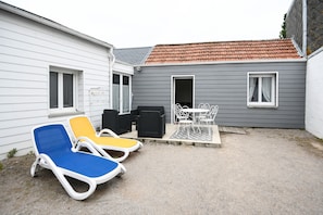 Un petit espace extérieur avec une table et des chaises, un coin salon abrité et un bâtiment doté d’un toit en tuiles.