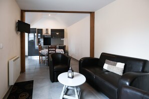 En moderne stue med sofa, stole, et lille bord og et tv ophængt på væggen.