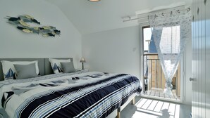 Et soveværelse med seng, natbord, lampe, loftlampe, et vindue med gardiner og en balkon.