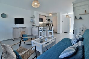 A modern living room with a sofa, chairs, a coffee table, a TV, and a kitchen area. - Maison les flots de port-mer, 2 min walk to Port Mer beach (Cancale)