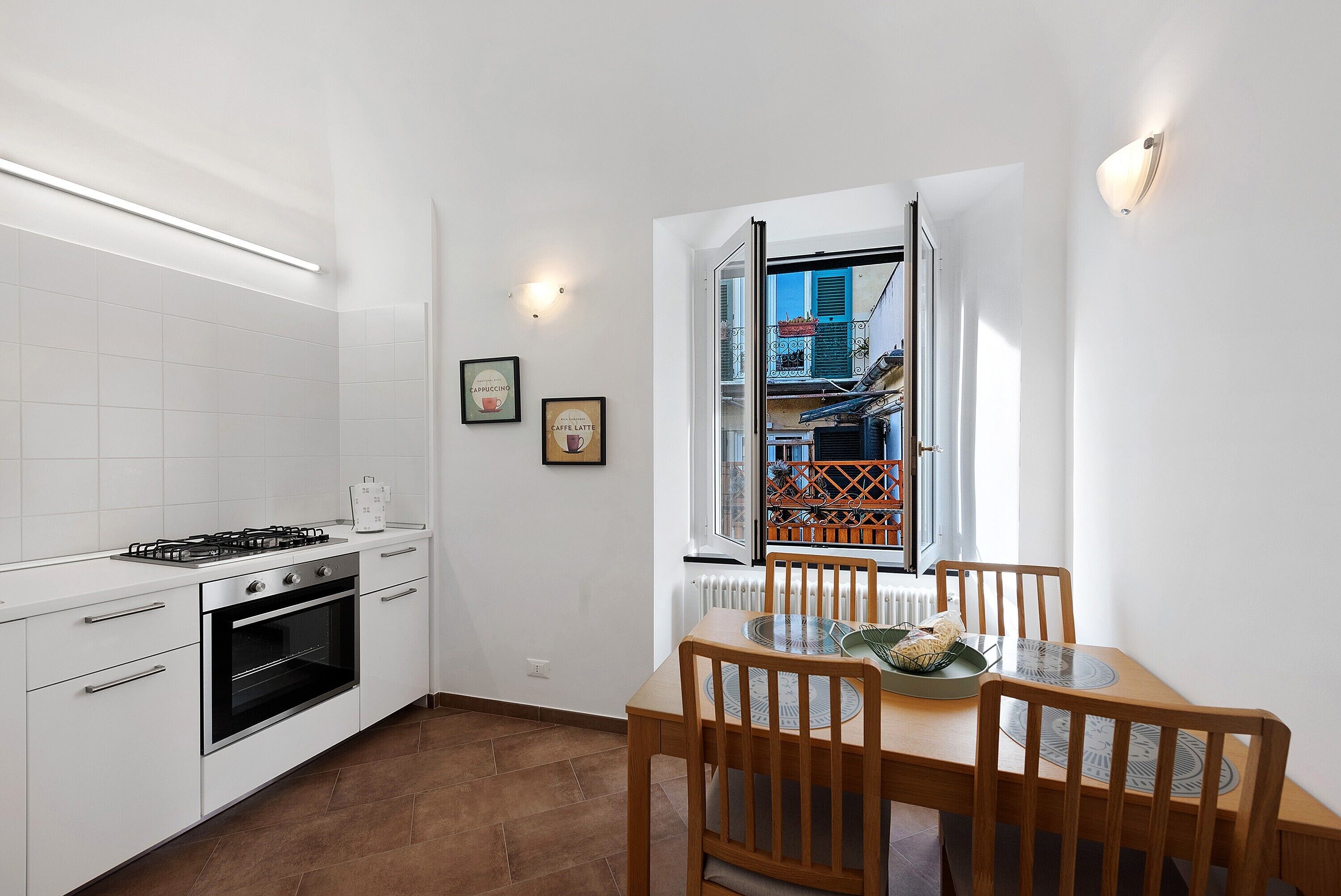 Una cocina con armarios blancos, una estufa y un comedor con mesa y sillas.