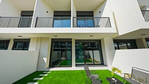 Een modern gebouw met twee verdiepingen, een plat dak, grote glasramen en een klein terras met een tafel en stoelen.