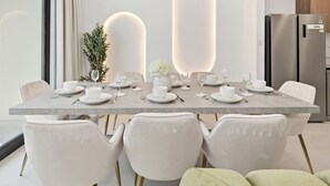 Een moderne eetruimte met een marmeren tafel voor zes personen, witte stoelen en een minimalistische inrichting.