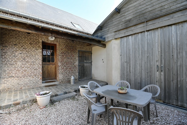 Une terrasse avec une table et des chaises, un bâtiment en briques et une cl ôture en bois.