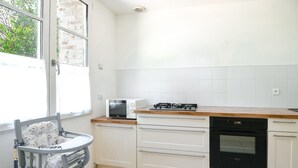 Eine Küche mit weißen Schränken, einer Mikrowelle, einem Backofen und einem Fenster mit Blick ins Grüne.
