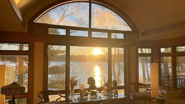Ein geräumiges Wohnzimmer mit großen Fenstern und Blick auf ein Gewässer, ausgestattet mit Sesseln und einem Couchtisch.