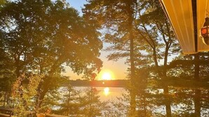 Ein Sonnenuntergangsblick von einem Balkon mit Geländer, mit Blick auf einen von Bäumen umgebenen See.