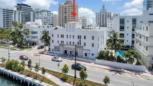 Un paisaje urbano costero con edificios modernos, un paseo marítimo y un edificio blanco destacado con una flecha roja que lo señala.