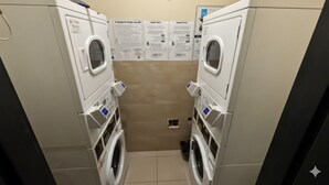 Un lavadero con dos lavadoras y secadoras, piso de baldosas y carteles informativos en la pared.