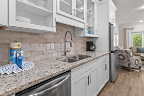 Eine moderne Küche mit weißen Schränken, einer Arbeitsplatte aus Granit, einem Edelstahl-Geschirrspüler und einem eingebauten Backofen.
