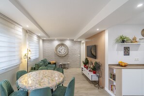 A modern living room with a round table, green chairs, a large clock, and a TV on the wall. - Cubo's Violeta Rural House Private pool / BBQ / Air conditioning / Free Wi-Fi (Coín)