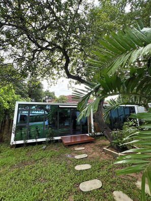 A modern house with a glass facade, surrounded by lush greenery and a tree.