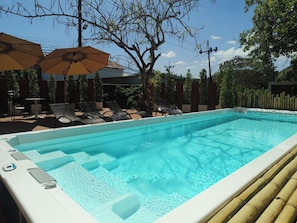 A rectangular swimming pool with a white edge, surrounded by lounge chairs and umbrellas.