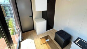 Una habitación compacta con puerta corredera que da a un área exterior, un pequeño rincón de descanso y un equipo de aire acondicionado integrado.